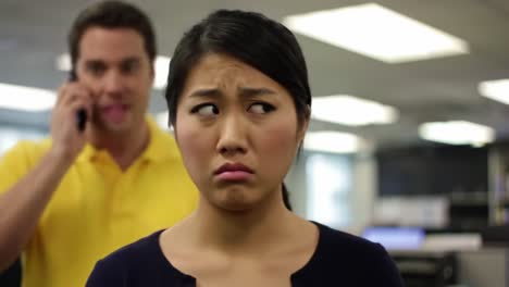 an employee reacts with discomfort as a co-worker talks loudly on the phone nearby. the office atmosphere is tense, highlighting workplace distractions.