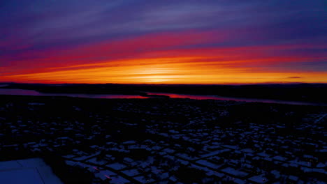 aerial drone view of a vivid, blazing sunset over a snowy residential neighborhood