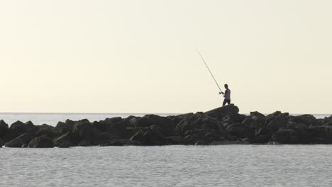 Junger-Mann,-Der-Im-Morgengrauen-Von-Felsen-Im-Meer-Fischt