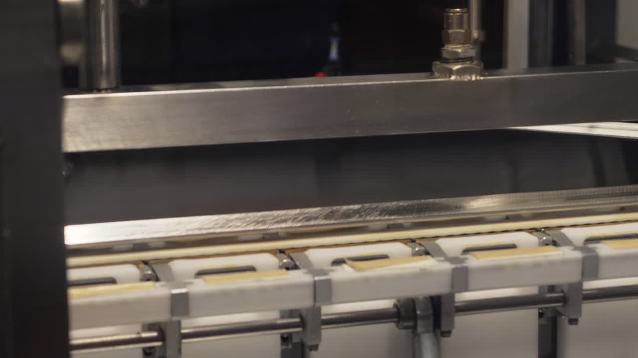 Static medium close-up shot of a factory machine folding triangular sugar candy onto moving bars along a stainless-steel conveyor in an automated confectionery production line