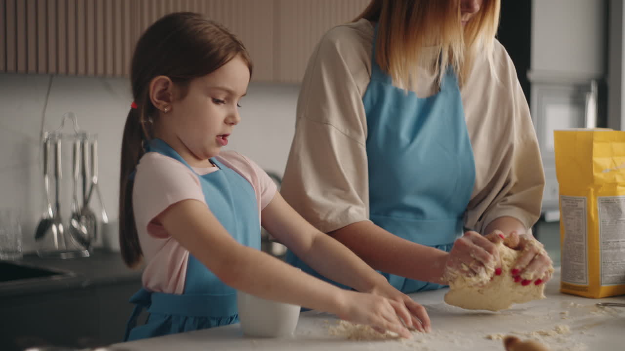 una niña linda está aprendiendo a cocinar amassando masa en la mesa de la cocina de la casa ayudando a su madre