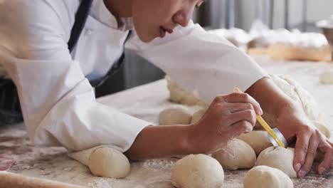 focused asian female baker working in bakery kitchen, cutting dough for rolls in slow motion