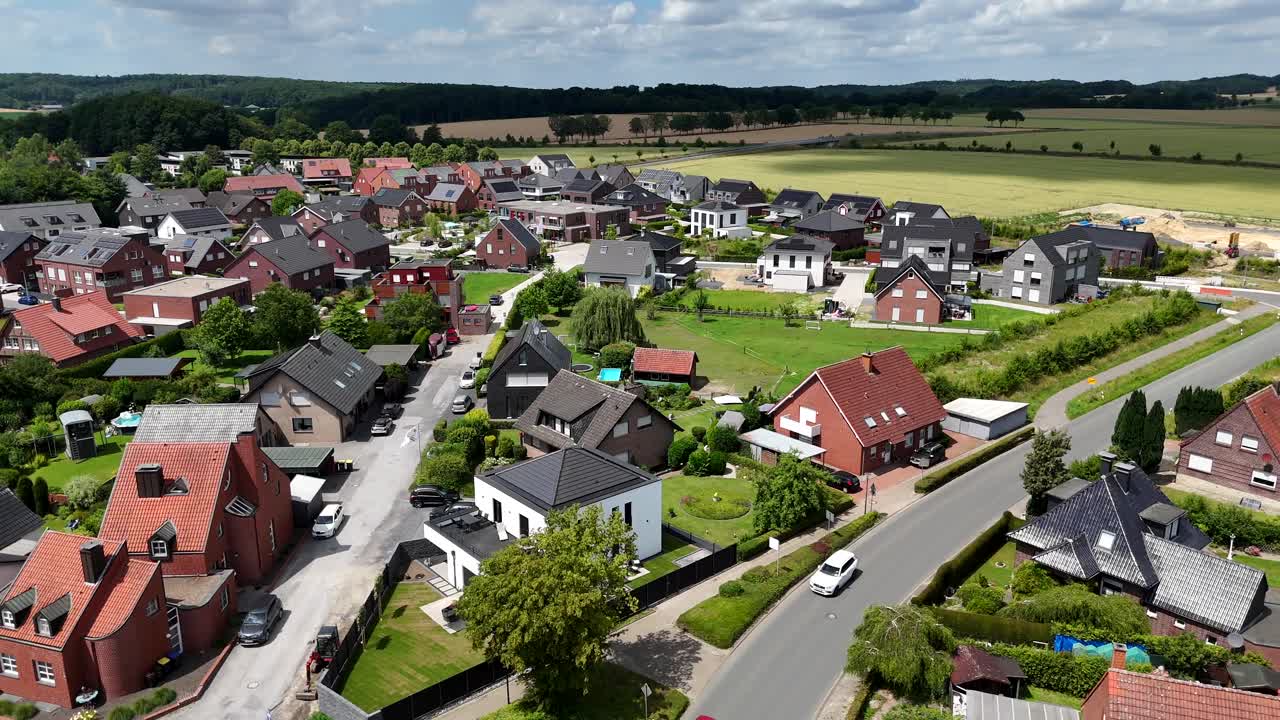 White Urban Quarter House with terrace and black roof in new build suburb of German town. Cloudy summer day in Small city. Forest trees and farm fields in distance. Traffic on road. Modern homes.