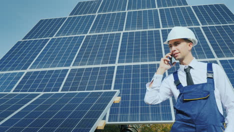 young engineer talking on the phone on the background of a large solar panel