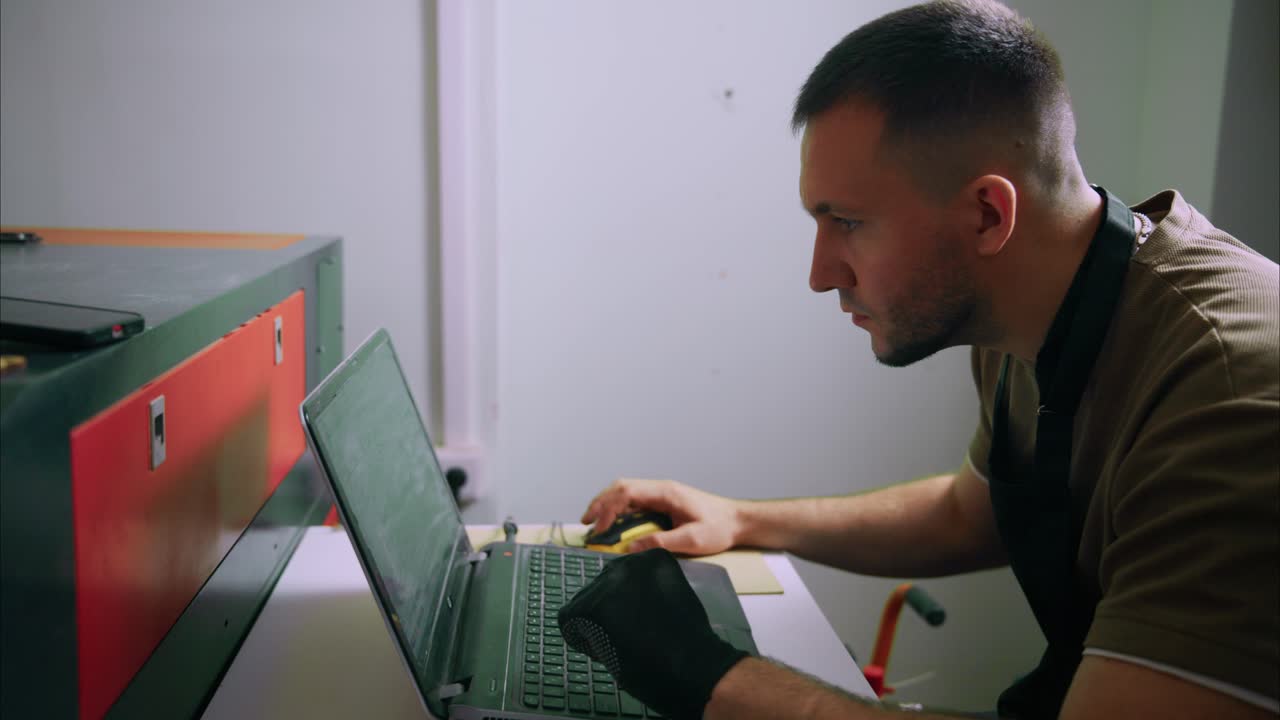 Man Working on Laptop Operating Laser Cutting Machine