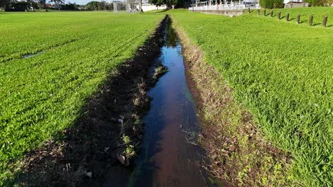 aerial footage of a water drainage channel cutting through lush green grass in a gold coast park