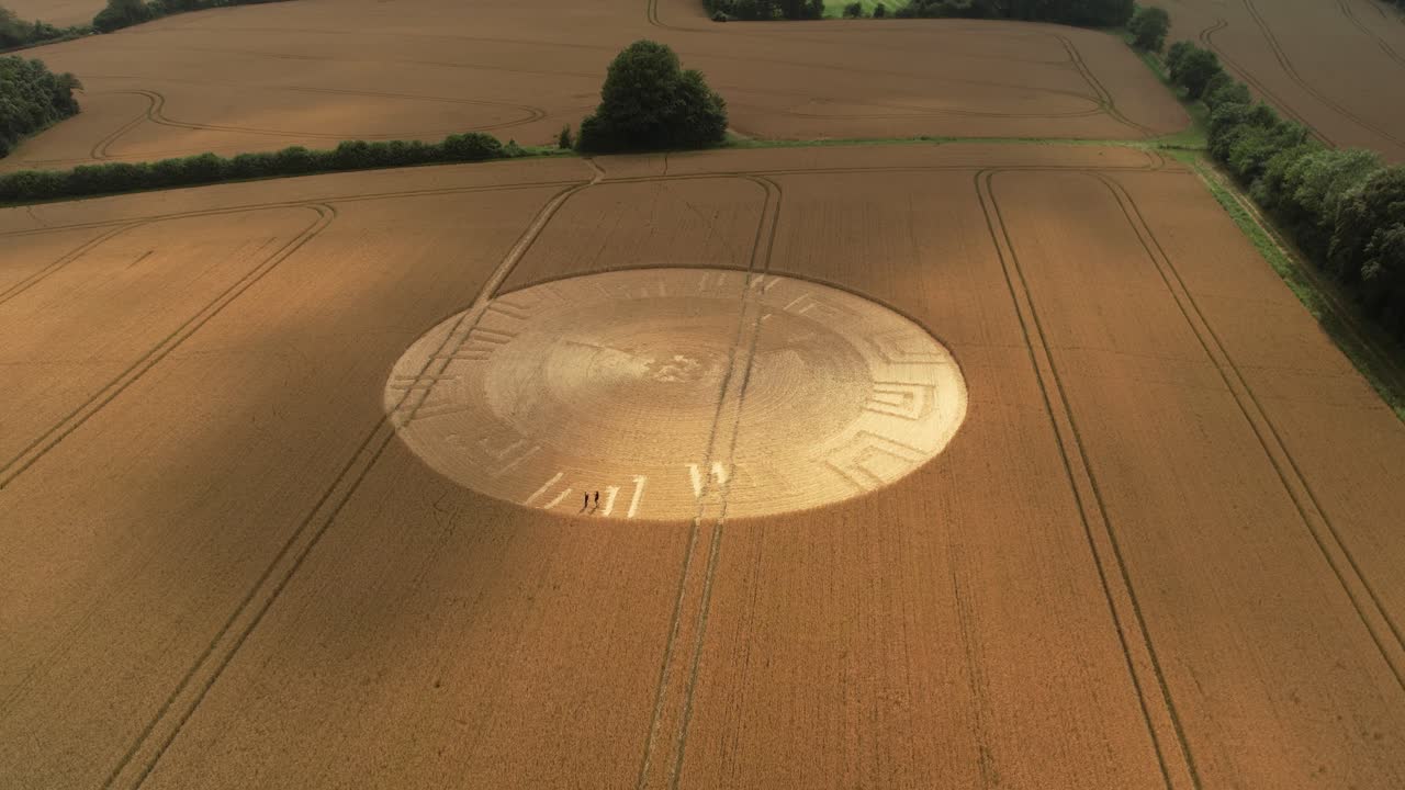 Aerial view towards plowed remains of golden crop circle formation shining on Wiltshire farmland