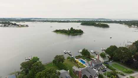 Aerial-view-of-a-private-island-over-a-coastal-town-with-sail-boats-and-vessels-over-bay-water-in-New-England