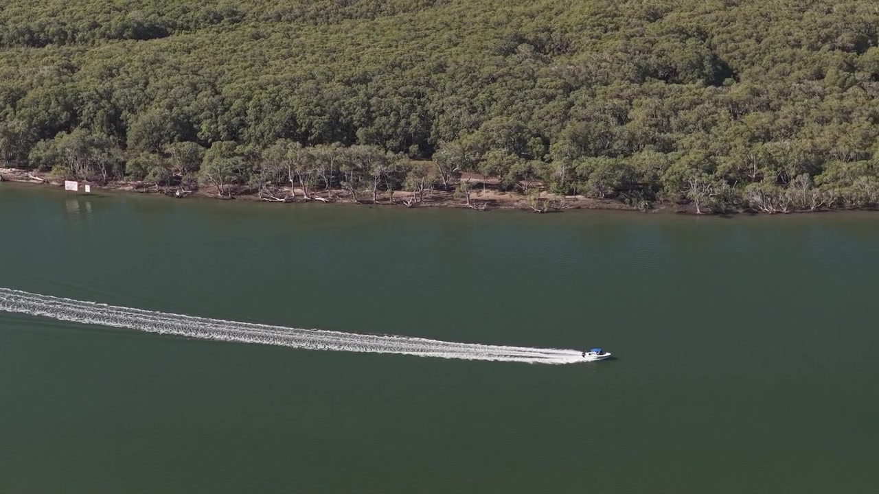 Perahu motor melintasi perairan dengan taman hijau subur dekat Paradise Point di Gold Coast Utara, Australia. Rekaman Pelacakan Udara.