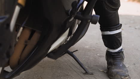 driver puts support and gets out of motorcycle on dirty road