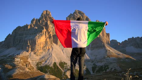 imágenes filmadas en rifugio auronzo, tri cine en las montañas de los dolomitas italianos con un hombre moviéndose y sosteniendo una bandera italiana y con hermosas montañas en el fondo, filmadas al amanecer en 4k