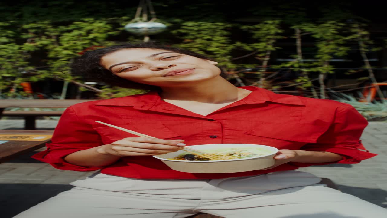 mujer comiendo fideos al aire libre
