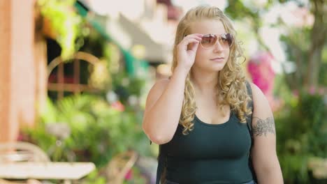 la chica camina por la acera del centro y ajusta las gafas de sol