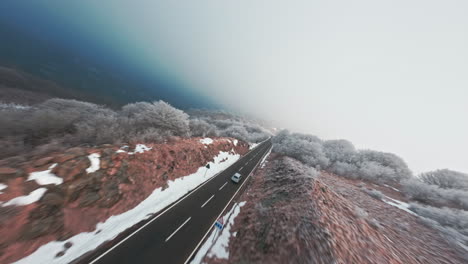 winding road through snow-covered mountains with an fpv drone flying overhead