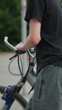 dos hermanos caminando uno al lado del otro, cada uno empujando sus bicicletas a través de un cruce de peatones, el fondo presenta una señal y vegetación borrosa y un edificio residencial en la distancia