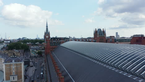 Low-flight-above-roof-of-St-Pancras-train-station-in-Camden-borough.-Heading-to-historic-brick-building-with-clock-tower.-London,-UK