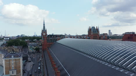 Vuelo-Bajo-Por-Encima-Del-Techo-De-La-Estación-De-Tren-De-St-Pancras-En-El-Distrito-De-Camden.-Dirigiéndose-Al-Histórico-Edificio-De-Ladrillo-Con-La-Torre-Del-Reloj.-Londres,-Reino-Unido