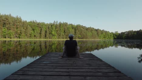 Lac-de-Lispach,-man-sits-back-with-arms-behind-looking-out-at-calm-reflection-of-lake