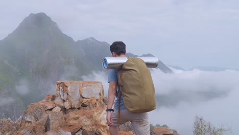 asian hiker male hiking to the top of foggy mountain and raising his hands for celebrating