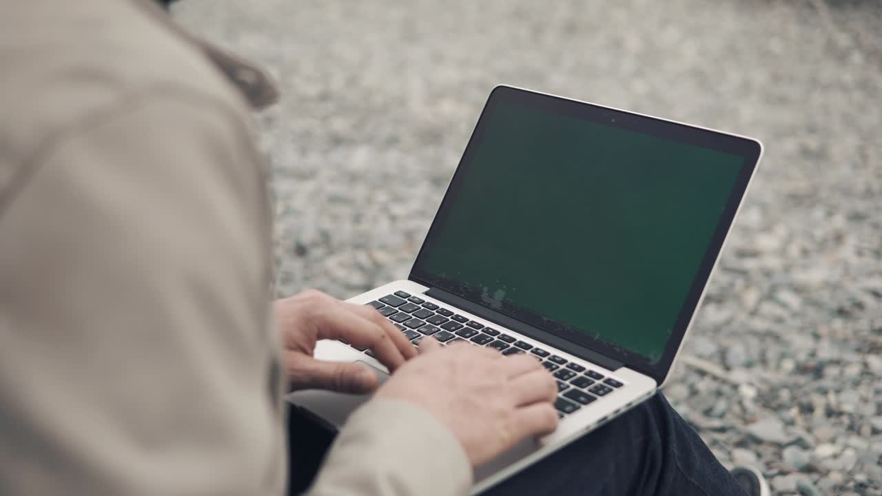 close up shot of a man's hands who work on a laptop outdoors among a rocky beach