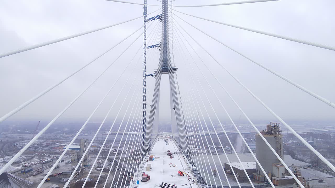 Drone video above snow-covered deck of Gordie Howe Bridge on cloudy winter day