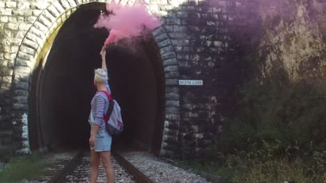 mujer con humo rosa en un túnel en las vías del tren