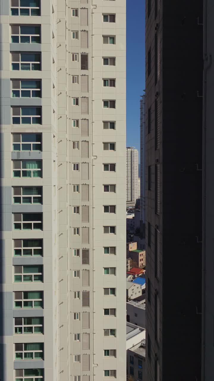 Plano vertical ascendente que revela la fachada de un complejo de apartamentos residenciales de varios pisos con un cielo azul despejado de fondo en una zona urbana de la ciudad de Daegu