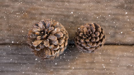 snow falling over two pine cones on wooden surface