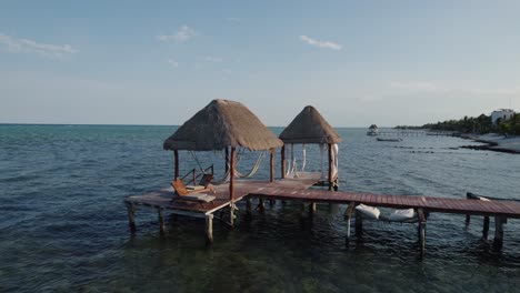 Aerial-of-wooden-pier-with-small-wooden-open-building-at-the-mexican-coastline-of-Alea,-Tulum,-Mexico