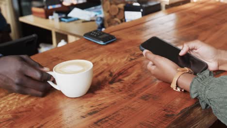 un barista afroamericano que sirve café a una cliente usando un teléfono inteligente, en cámara lenta.