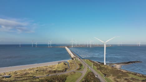 Toma-Aérea-En-Cámara-Lenta-De-Turbinas-Eólicas-Y-Una-Carretera-En-Una-Zona-Costera-De-Los-Países-Bajos-En-Un-Hermoso-Día-Soleado