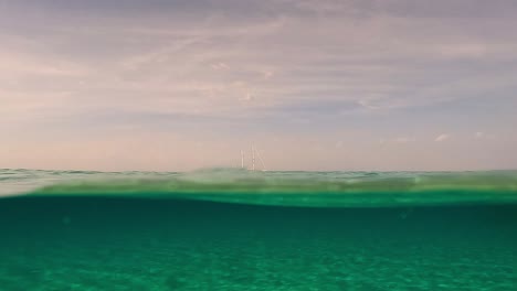 split underwater surface perspective of sailing ship moored on the horizon with sails lowered