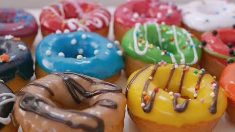 las rosquillas están dispuestas en una caja blanca en varias filas, decoradas con esmaltado de frutas. en la parte superior del esmaltado hay chocolate blanco-oscuro y salpicaduras de pastelería. dulces de primer plano. concepto de obesidad