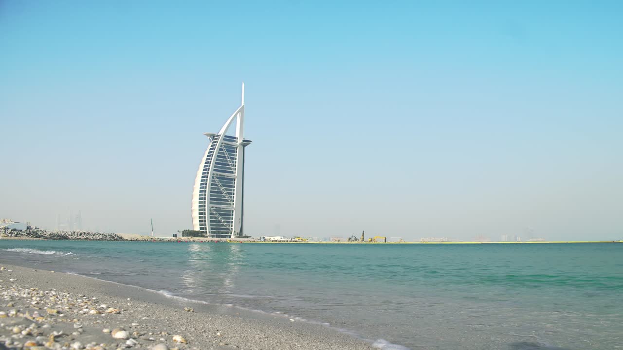 Burj al Arab visto dalla spiaggia di Jumeirah, spiaggia ventosa e tranquilla, onde, cielo blu, oceano blu ecc.