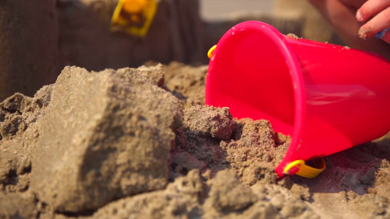 백그라운드에서 모래 성을 짓는 아이와 함께 모래 해변에 빨간 양동이