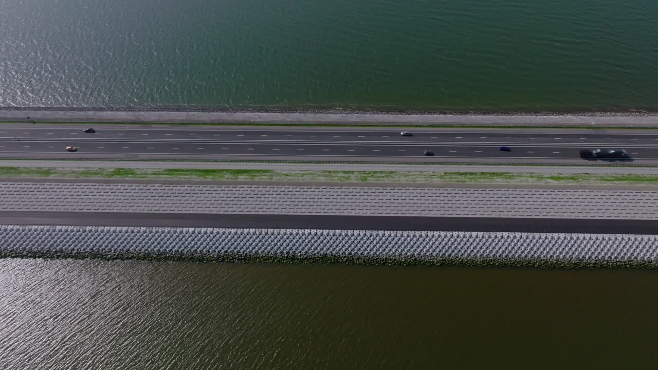 Aerial pan left showing the Afsluitdijk highway stretching across the sea with vehicles driving between two bodies of water