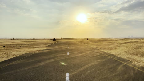 Highway-road-in-the-middle-of-the-desert-while-the-wind-bows-the-fine-sand-at-sunset