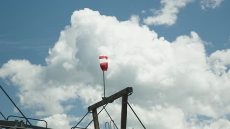 watch the graceful dance of a white and red windsock against a vast white cloud