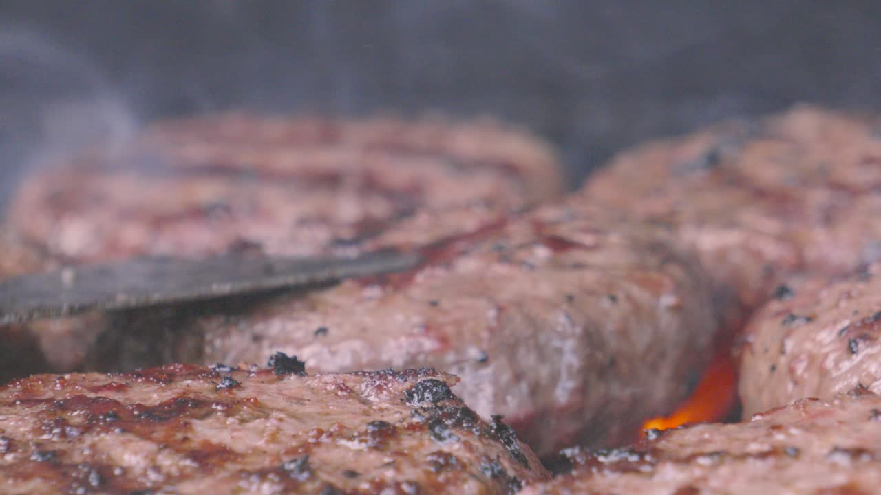 Multiple Burgers Being Flame Grilled Outside on Smoking Hot BBQ with Chef Flipping Over Patty in Slow Motion. Close Up Food Cooking Outside.