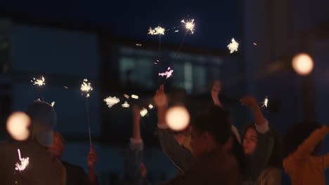 happy friends holding sparklers celebrating new years eve on rooftop at sunset having fun enjoying holiday party celebration