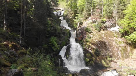 high waterfall falling under on rock and a wooden bridge on the top of the cascade