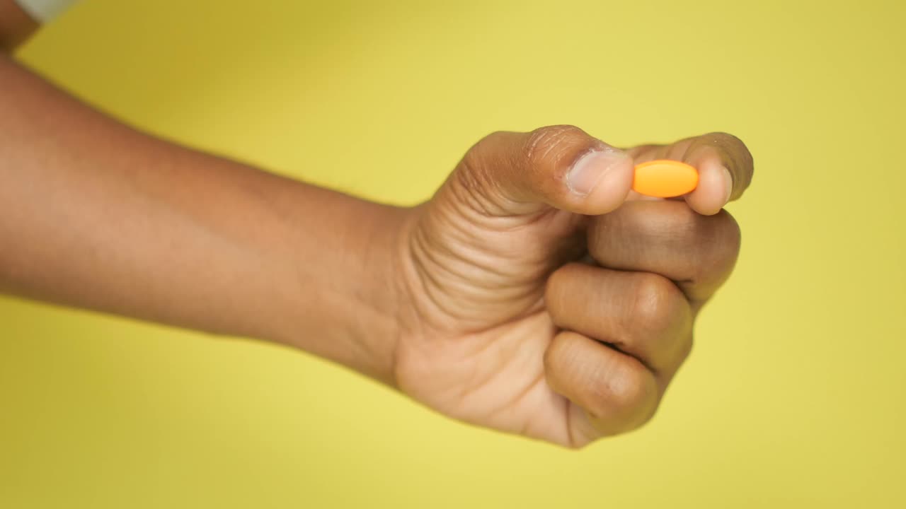 Hand holding an orange pill