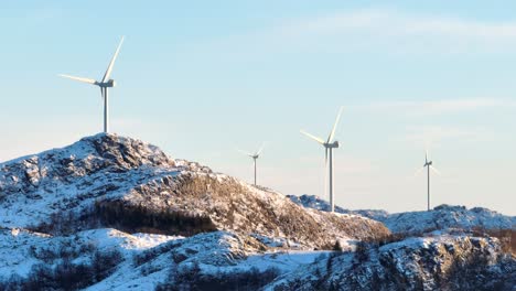 Turbinas-Eólicas-En-La-Cima-De-Colinas-Montañosas-Cubiertas-De-Nieve-En-Un-Soleado-Día-De-Invierno,-Estableciendo-Disparos-De-Drones