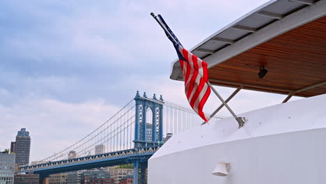 american flag waving on the modern boat swaying on the water. spectacular manhattan bridge at backdrop