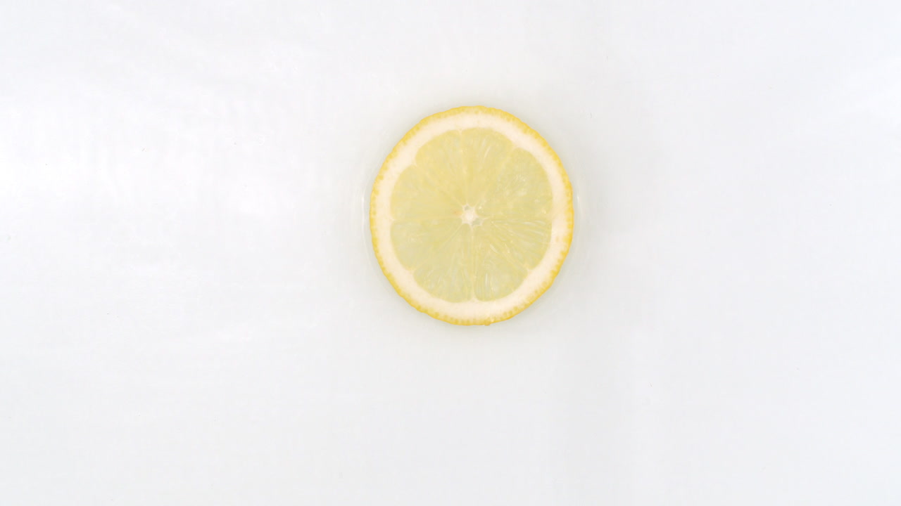 Slow motion water splash on one slice of lemon lying on a white background in water