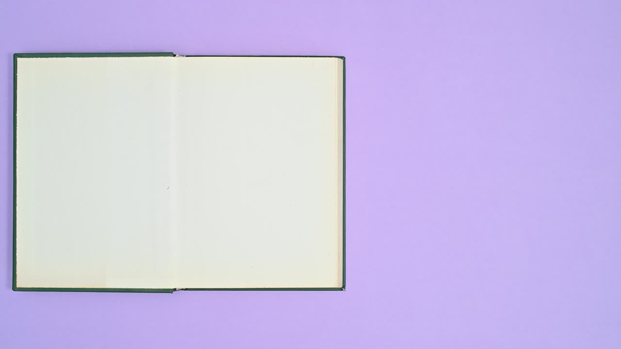 Hand put dark green hardcover retro vintage book on purple theme and book opens. Stop motion flat lay