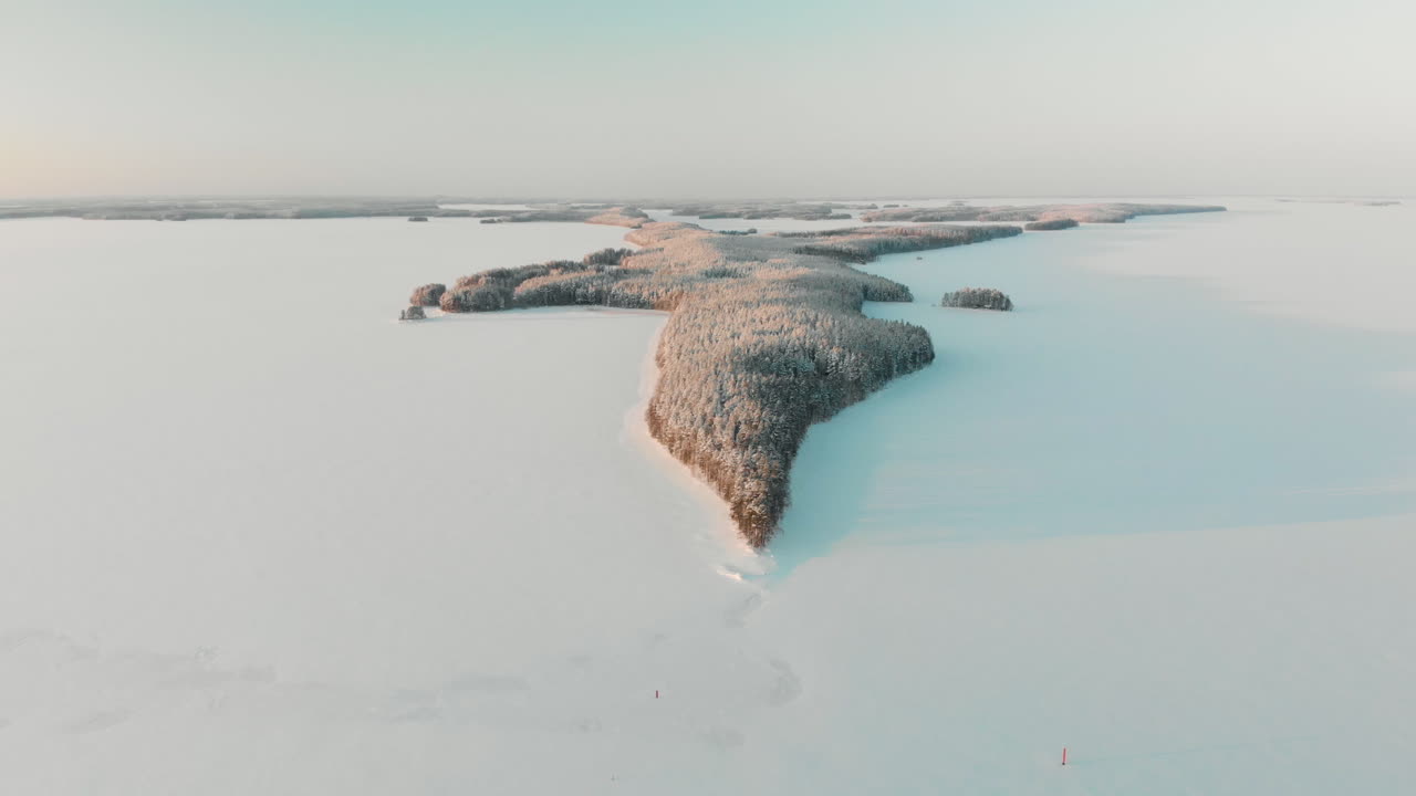 Aerial, tracking, drone shot, of Vuoniemi cape, in the middle of snowy lake Saimaa, full of pine tree forest, at sunset, on a sunny, winter evening dusk, in North Karelia, Finland