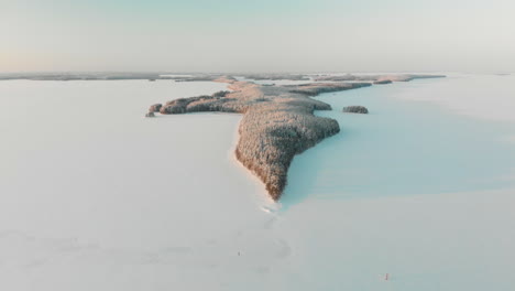 aerial, tracking, drone shot, of vuoniemi cape, in the middle of snowy lake saimaa, full of pine tree forest, at sunset, on a sunny, winter evening dusk, in north karelia, finland