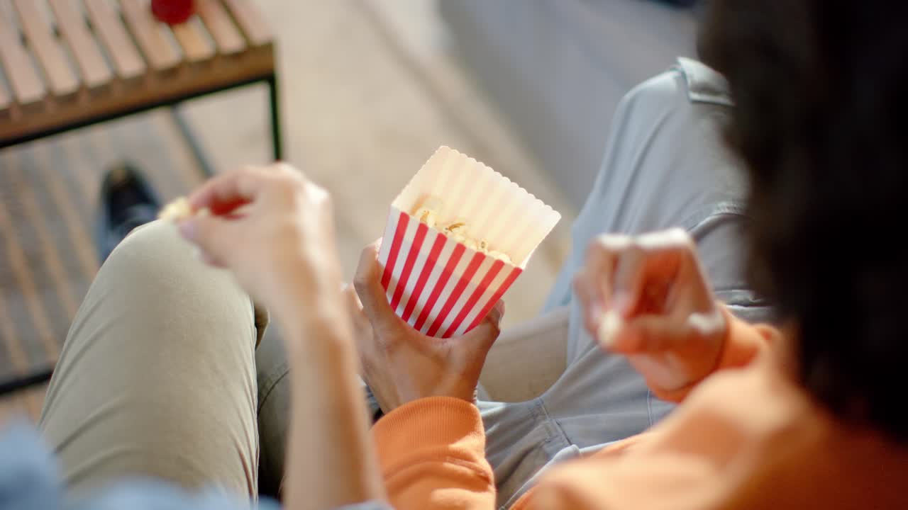 Forskellige venner deler popcorn og skiftes til at snuppe dem fra sofaen derhjemme, mens den ene ven rækker ud.