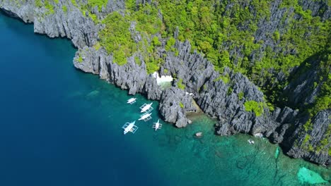 panorama aerial view of secret beach in el nido with tour boats against tropical lagoon hidden behind rock formations, matinloc - philippines